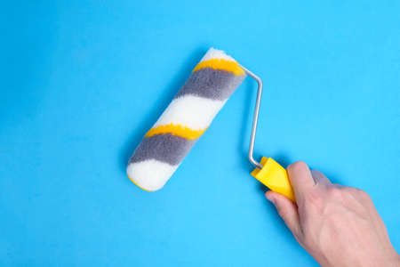 Paint roller in hand for painting walls and repairs on blue backgroundの写真素材