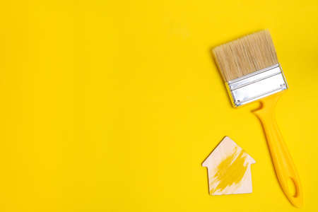 Bristle paint brush for painting and repairing, as well as a figurine of a house on a yellow backgroundの写真素材