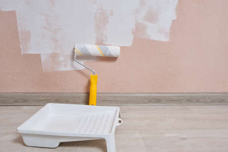 Painting tray with white paint and painting roller against pink wall painted with white paintの写真素材