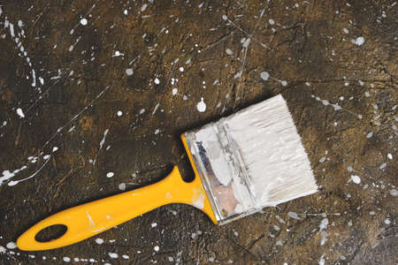Paint brush smeared with gray paint on a concrete floor stained with paint dropsの写真素材