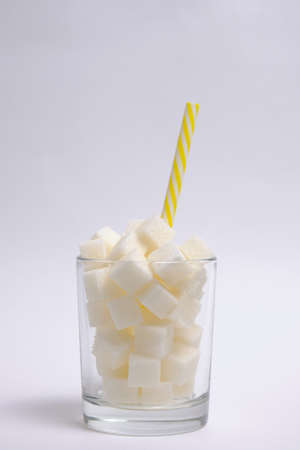 Glass with refined sugar cubes and a drinking tube on a white backgroundの写真素材