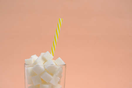 Glass with refined sugar cubes and a drinking tube on a beige backgroundの写真素材