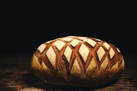 Loaf black rye bread sprinkled with flour on rustic wooden dark background