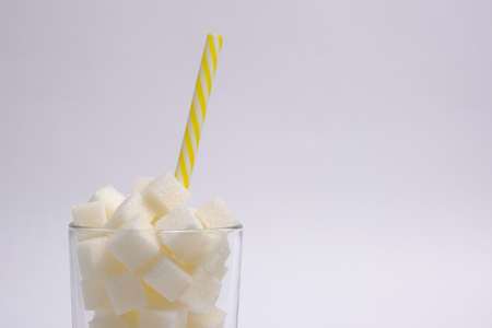 Glass with refined sugar cubes and a drinking tube on a white backgroundの写真素材