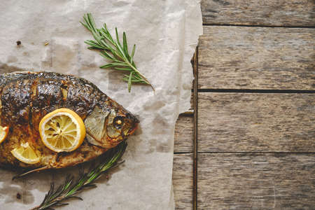 Baked fish cooked on parchment paper with spices, lemon and rosemary on a wooden backgroundの写真素材