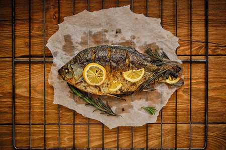 Baked fish cooked on parchment paper with spices, lemon and rosemary barbecue grill with wooden backgroundの写真素材