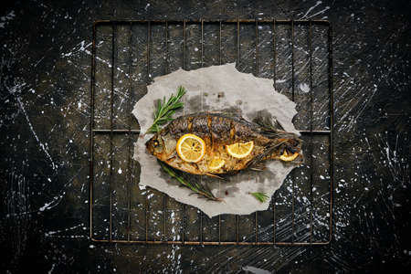 Fish baked in oven with lemon and rosemary on parchment paper, laid out on grate dark background