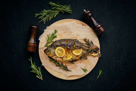 Baked fish in oven with lemon and rosemary laid out cutting board and parchment paper.On dark background with two strawsの写真素材