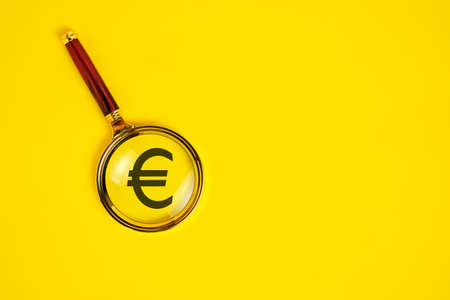 Euro symbol under magnifying glass, on yellow background
