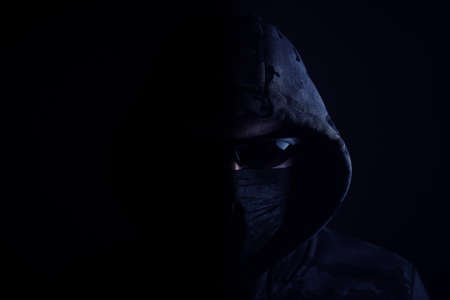 Stylish man in dark hoodie with black glasses and mask dark background, hacker, attacker and banditの写真素材