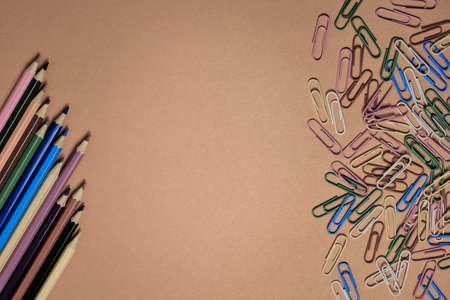 Colored pencils and stationery multi-colored paper clips on a brown backgroundの写真素材