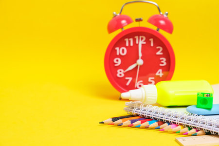 Red alarm clock and school supplies yellow background.Preparing child for schoolの写真素材
