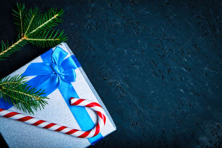 Christmas gift box tied with blue ribbon with bow with green Christmas tree and caramel on dark backgroundの写真素材