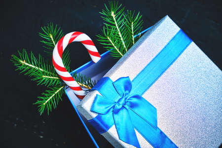 Christmas gift box tied with blue ribbon with bow with green Christmas tree and caramel on dark...