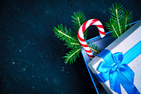 Christmas gift box tied with blue ribbon with bow with green Christmas tree and caramel on dark backgroundの写真素材