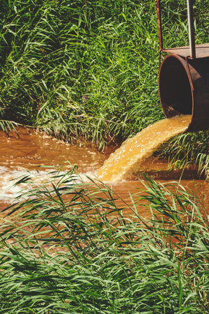 Industrial waste in the form of orange water flowing from pipe into riverの写真素材
