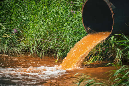 Industrial waste in the form of orange water flowing from pipe into riverの写真素材