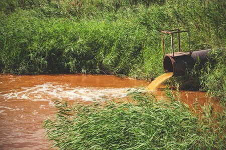 Industrial waste in the form of orange water flowing from pipe into riverの写真素材
