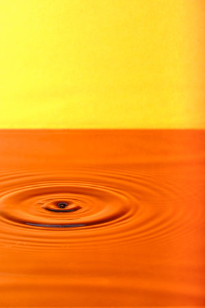 Splash drop of water with diverging water circles, on orange backgroundの写真素材