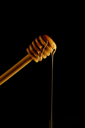 Wooden spoon for honey on black background and liquid fresh honey flowing down itの写真素材