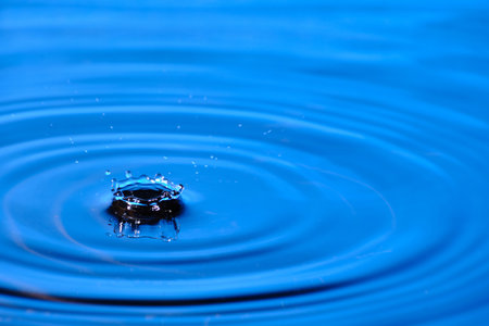 Splash drop of water with diverging water circles, on blue backgroundの写真素材