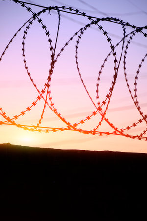 Fence with barbed wire background bright red setting sunの写真素材