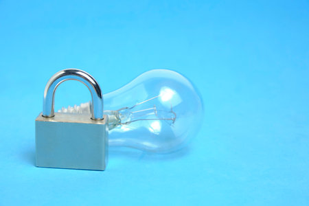Incandescent lamp and lock on blue background.Concept of power outageの写真素材