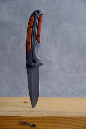 Folding knife for survival stuck wooden beam, on dark background