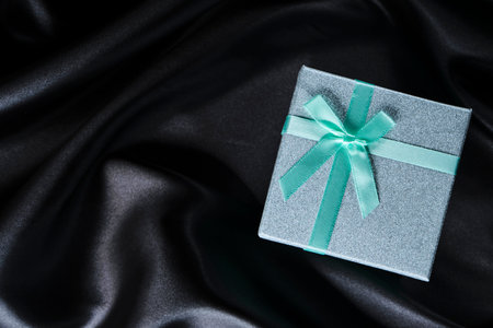 Green gift box with bow background with black silk fabricの写真素材