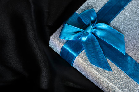 Silver gift box with blue bow background black silk fabricの写真素材