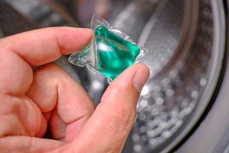 Washing capsule in hand against background drum washing machine
