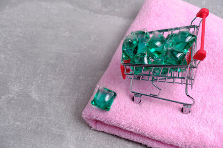 Shopping cart filled with laundry capsules stands on pink, terry towel
