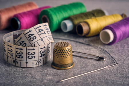 Sewing kit of needle, thimble, thread and measuring meter.On gray concrete table top