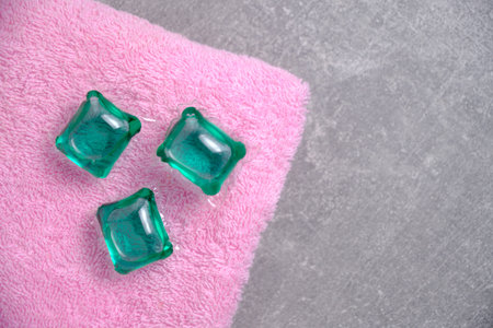 Green capsules for washing clothes on terry, pink, clean towel.On concrete backgroundの写真素材