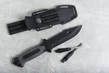 Tactical knife, scabbard and flint with mirror on grey background