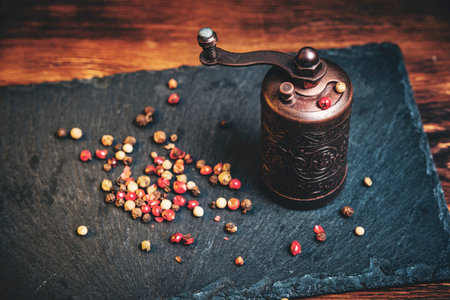 Old metal pepper and spice mill on slate tiles, on a wooden background