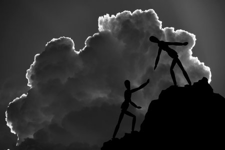 Two silhouettes mannequin climb mountain, one helping other, extending helping handの写真素材