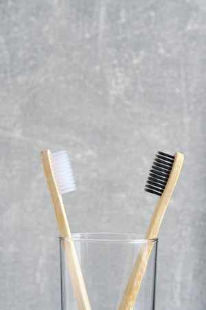Two wooden toothbrushes with black and white bristles in a glass in bathroom