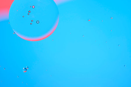 Macro photo with circles oil droplets water surface. Abstract blue and red background with oil bubblesの写真素材