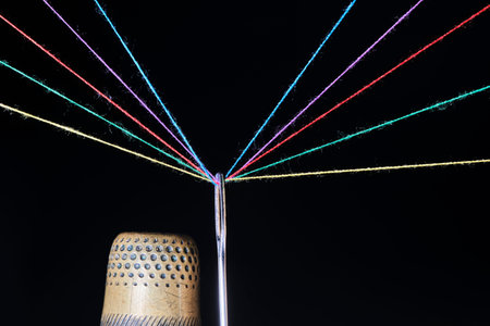 Thimble, eye sewing needle and multicolored threads passed through it black background