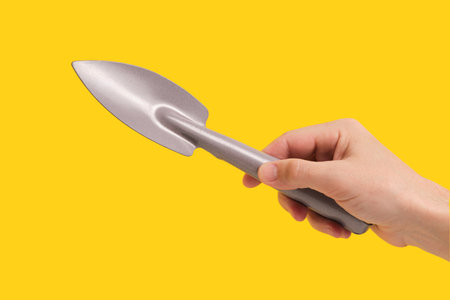 Planting scoop in hand yellow background for gardeners