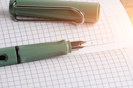 Fountain pen lying notebook with checkered pages is illuminated by bright sunlightの写真素材
