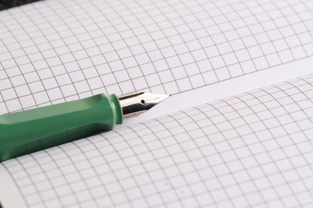 Green fountain pen lies on white sheets checkered notebook