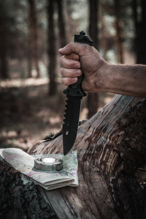 Hunting knife in forest with a compass and a map in hand