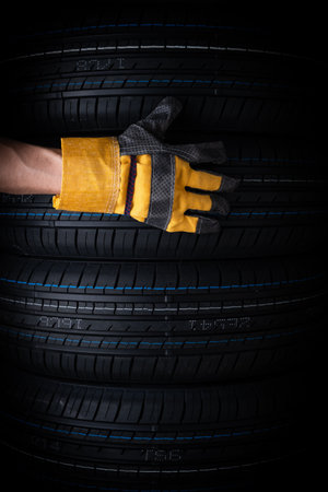 Hand in yellow glove with car tires on black background, closeup