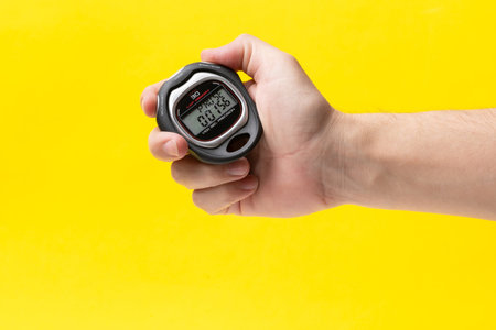 Man hand holding stopwatch on yellow background, closeup. Time management conceptの写真素材