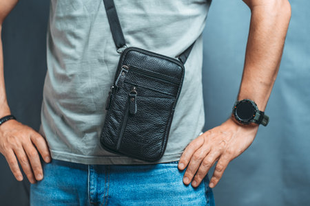 Men's hand holding a black leather handbag on a blue background