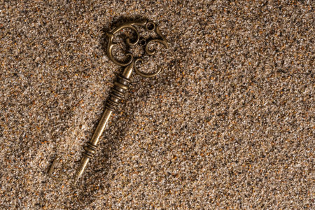 Old key on sand background. Top view. Copy space for text.