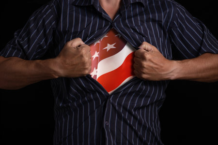 Man tears off shirt with U.S. flag underneath, symbolizing patriotism and strengthの写真素材