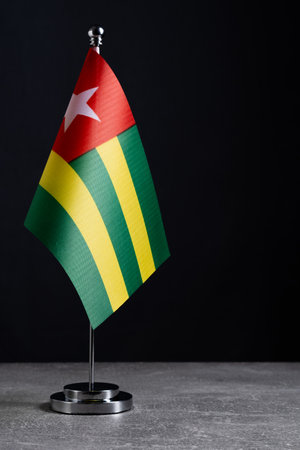 Small flag of Togo on a stand against a dark background.の写真素材
